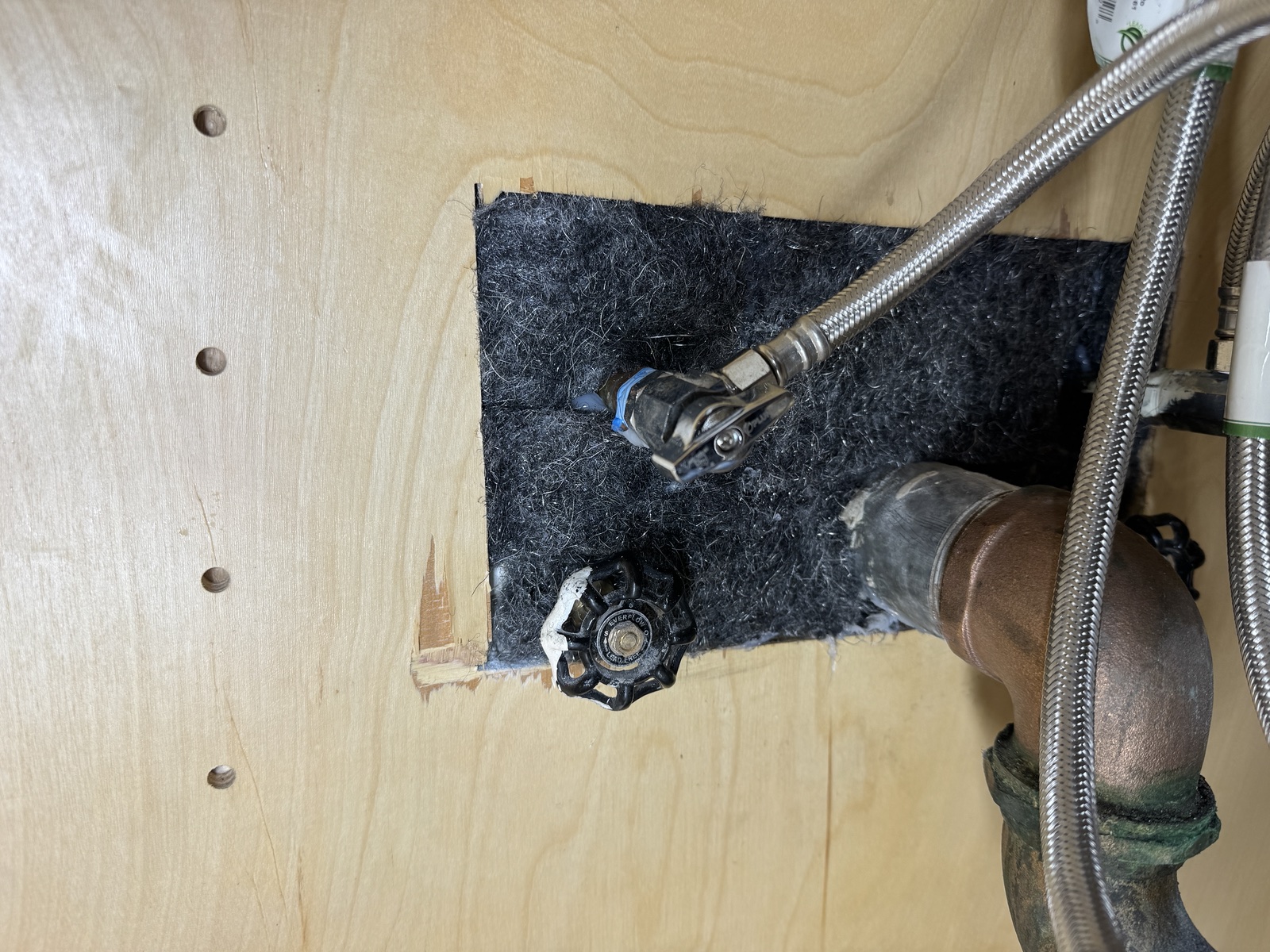 Dark sealing material fitted around plumbing penetrations in a cabinet